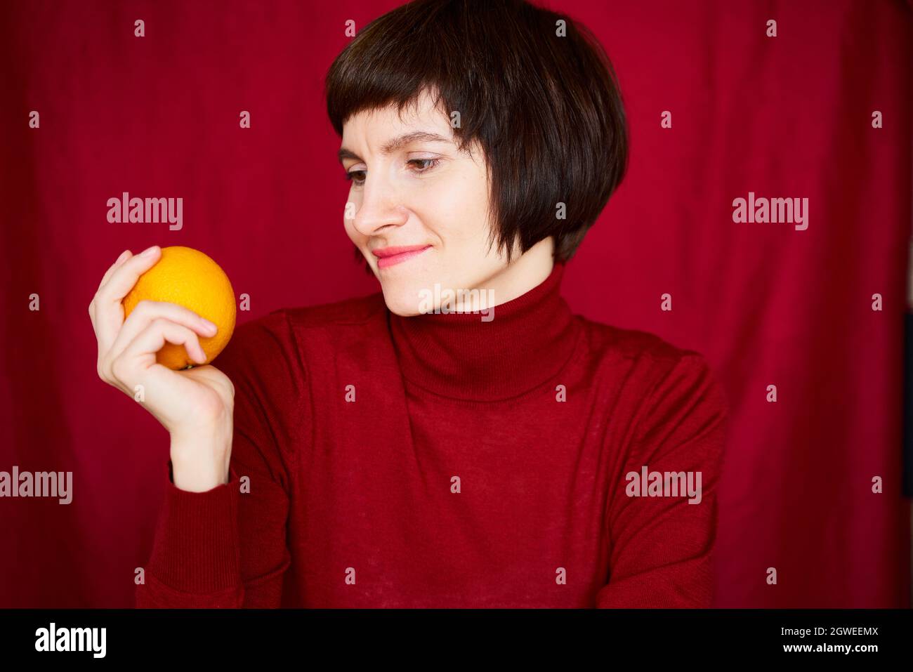 Smiling Mature Brunette Woman Looking At Orange Fruit In Hand, Close-up Face Portrait. Generation X, Stock Photo