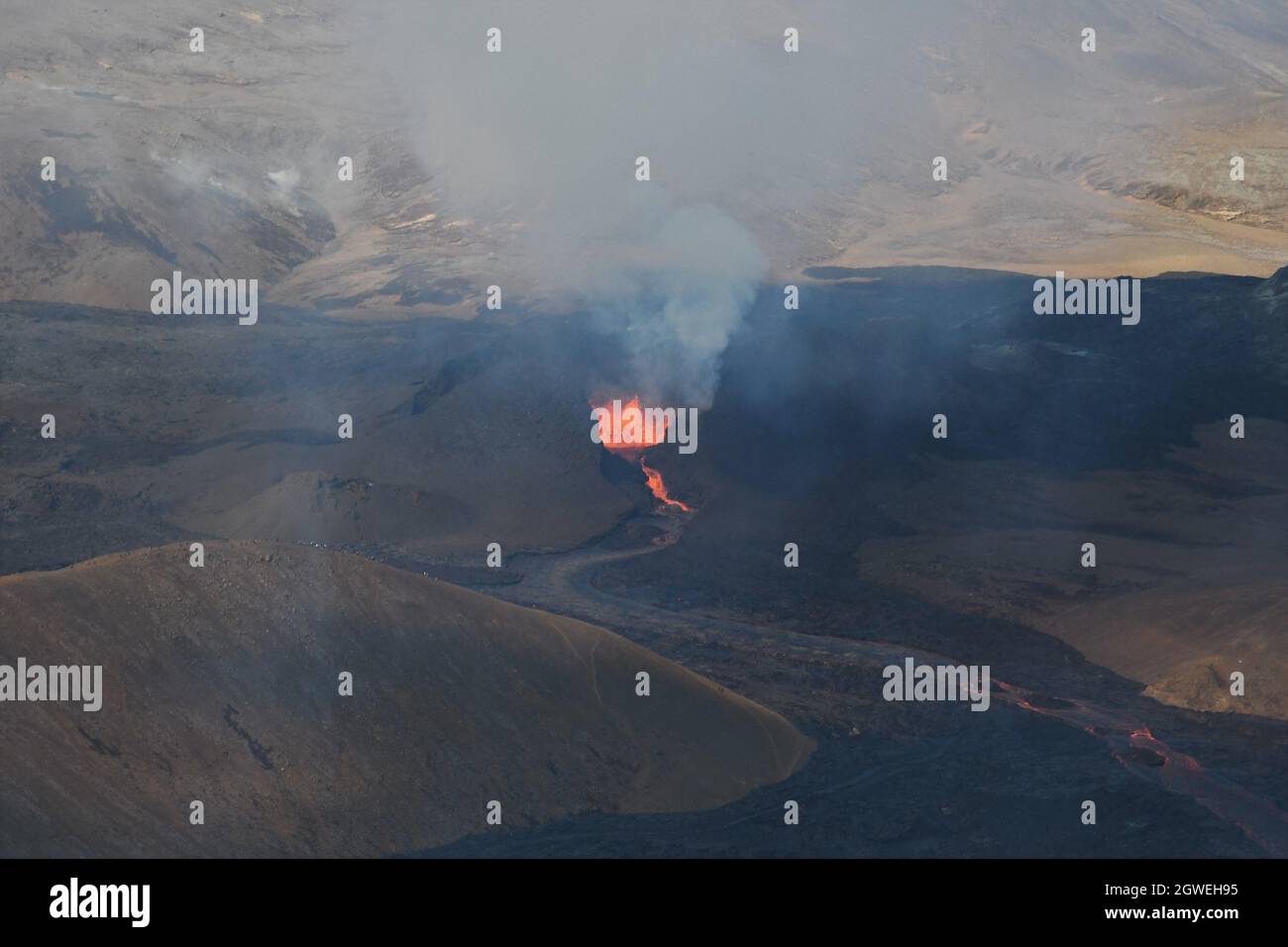 The lava field at Fagradalsfjall, Iceland. Active vent with molten lava erupting and volcanic gas rising. Black lava and blue sky. Aerial image. Stock Photo