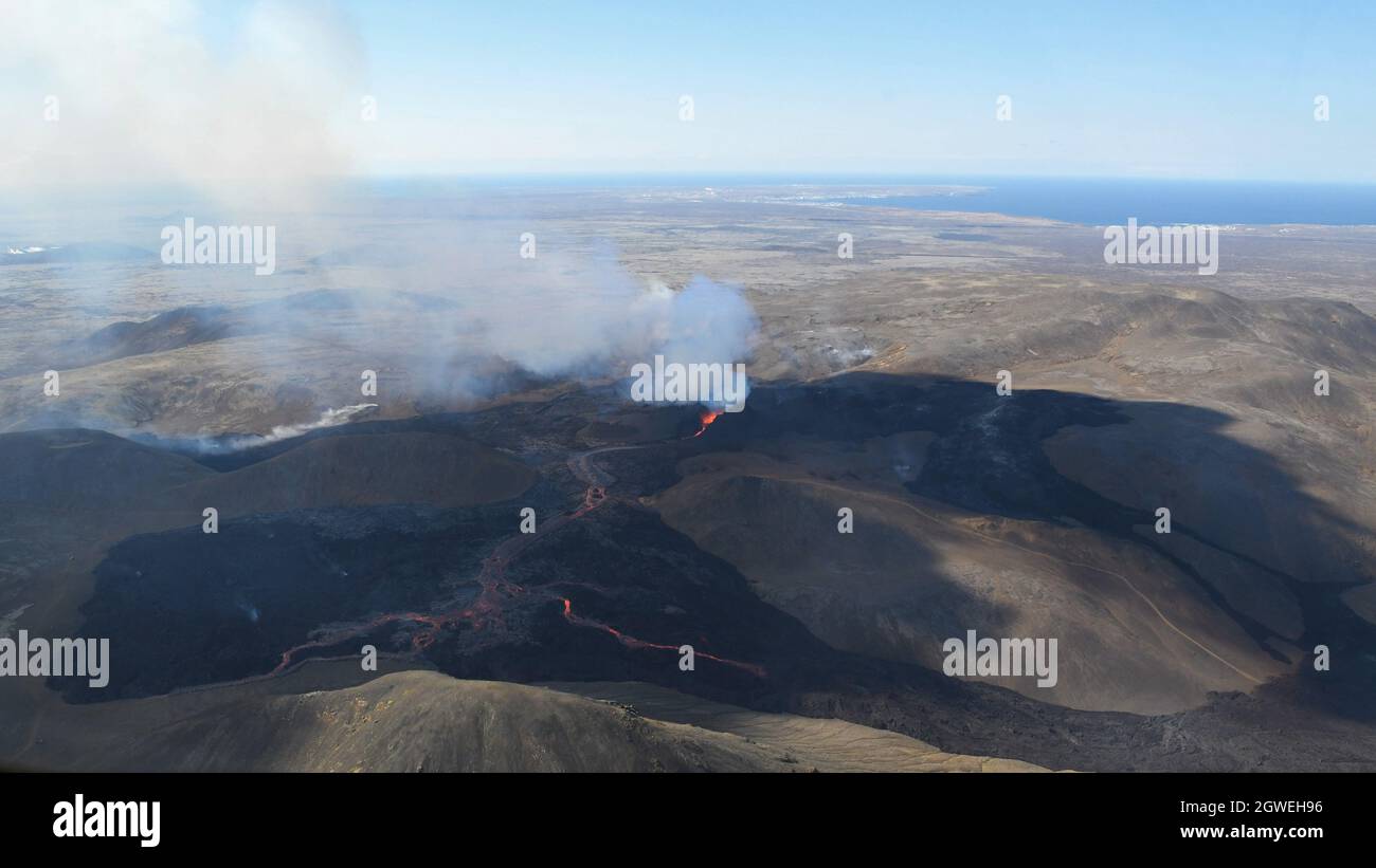 The lava field at Fagradalsfjall, Iceland. Active vent with molten lava erupting and volcanic gas rising. Black lava and blue sky. Aerial image. Stock Photo