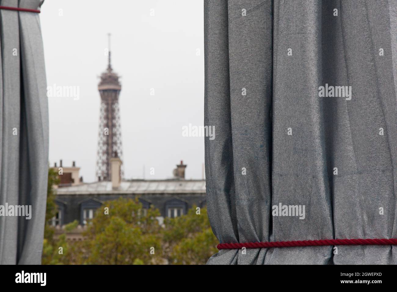 Paris, France, 3 October 2021: Heavy rain on the final day of the Arc de Triomphe Wrapped by Christo and Jeanne-Claude did not keep the crowds away. With rain macs and umbrellas, tourists and art lovers flocked to the Place Charles de Gaulle, which has been pedestrianised for the weekend. The Eiffel Tower was in the distance with it's top in the clouds. Anna Watson/Alamy Live News Stock Photo
