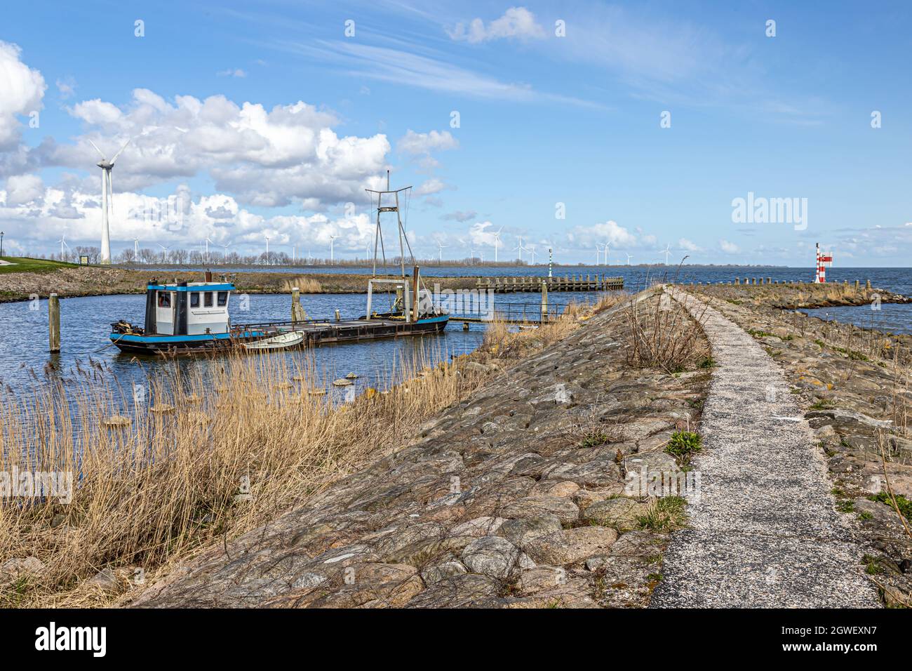 Entrance to Oosterhaven, city harbor with its dike, gates and a small anchored boat, horizon, windmills and blue sky in the background, sunny day at M Stock Photo