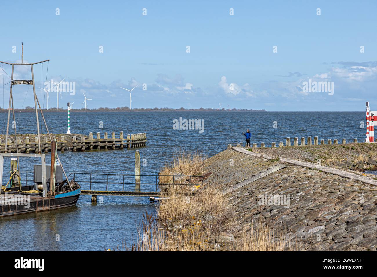Entrance to Oosterhaven, the city harbor with its dike, floodgates, horizon, windmills and blue sky in the background, tourist woman standing, sunny d Stock Photo