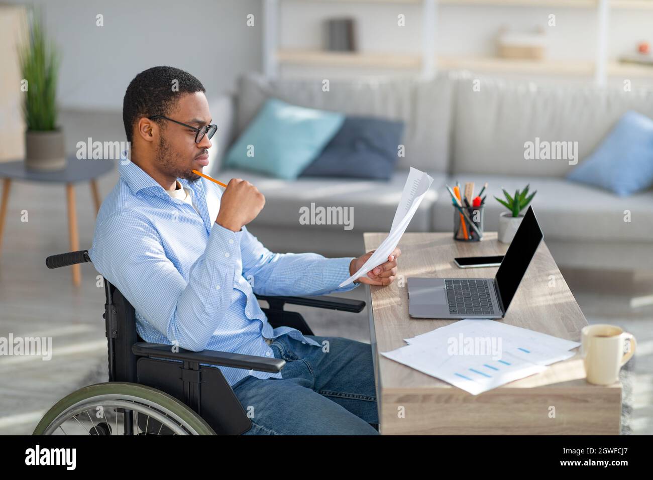 Focused black disabled man in wheelchair working with documents, using