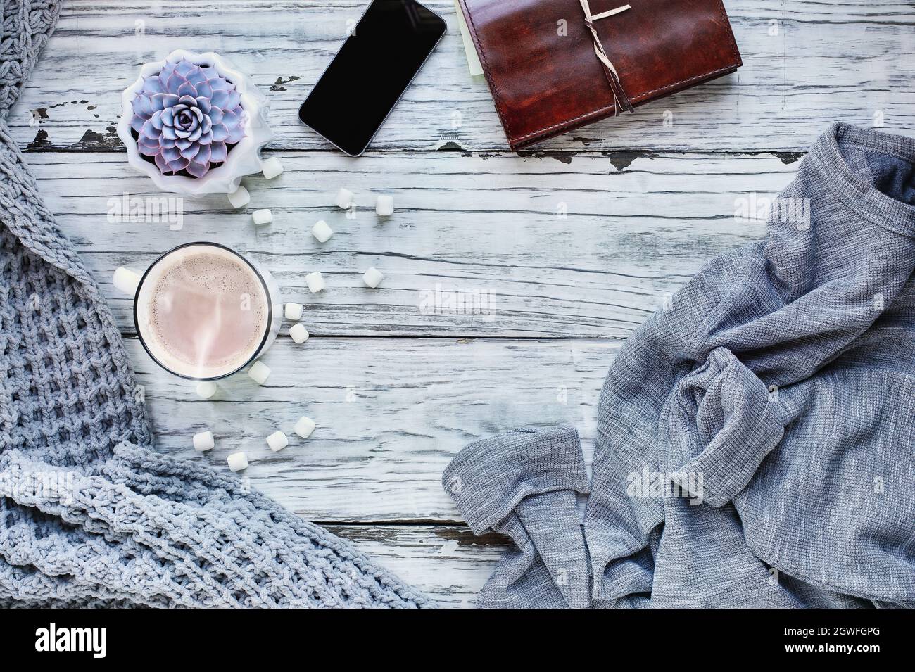 Autumn or winter background shot from top view with hot cocoa, houseplant, cell phone, book, throw blanket and sweater over rustic wood table Stock Photo