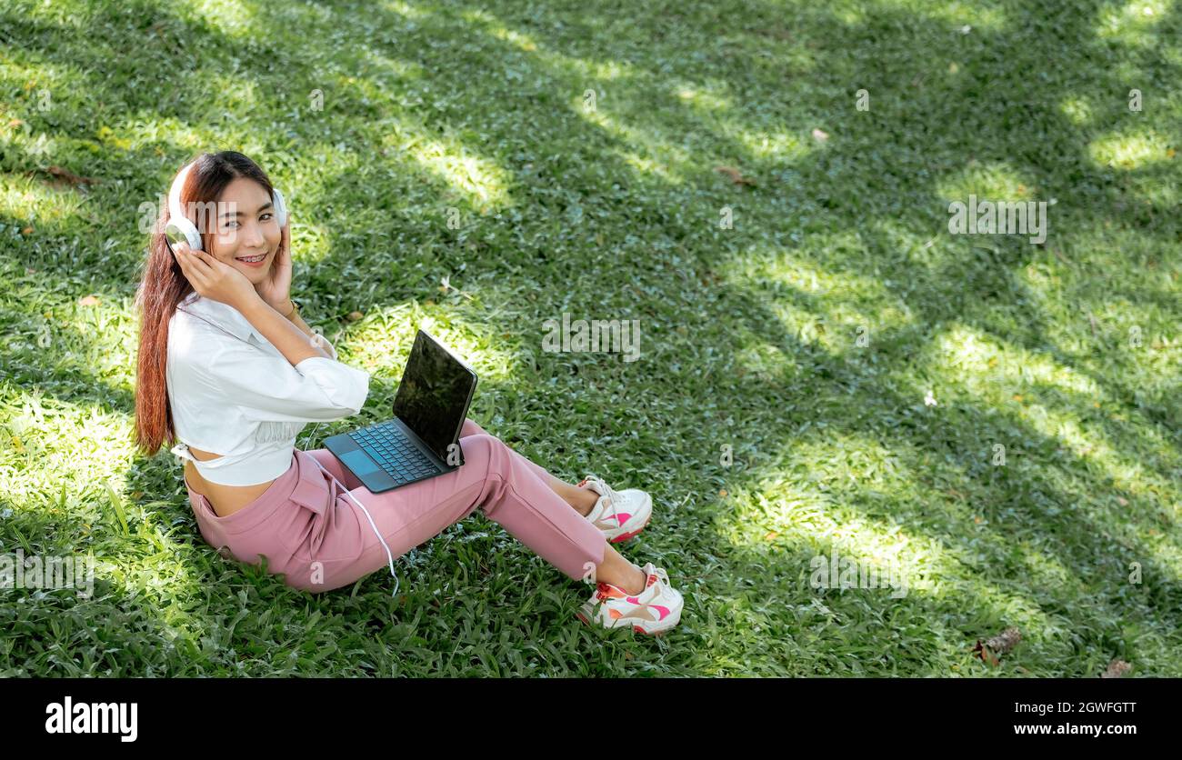 Happy student e learning with headphones and tablet at the park in a campus Stock Photo