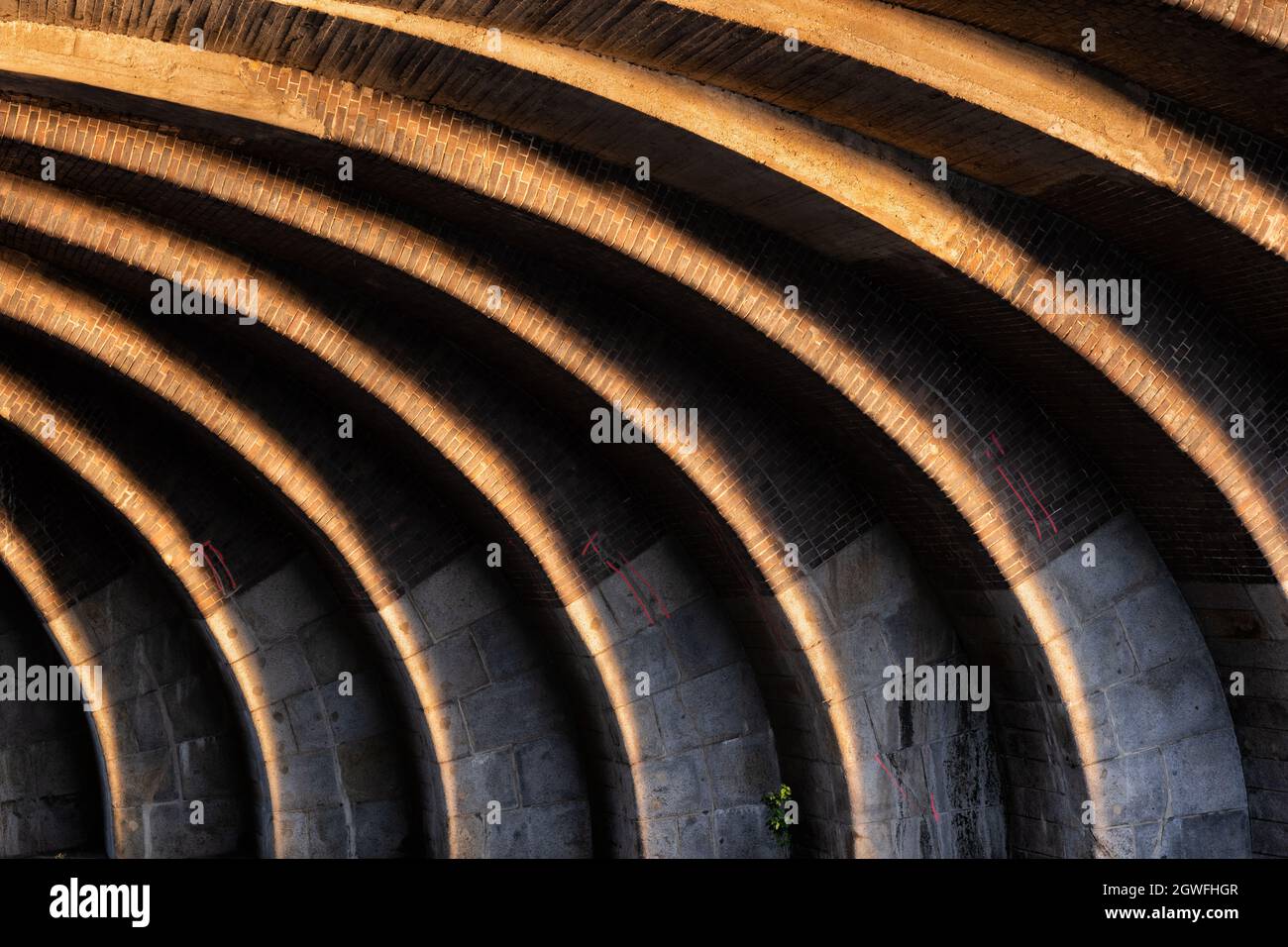 Abstract sunlit curved contrasting lines under the old railway bridge at sunset, arch brick and stone structure, light and shadow play in Berlin, Germ Stock Photo