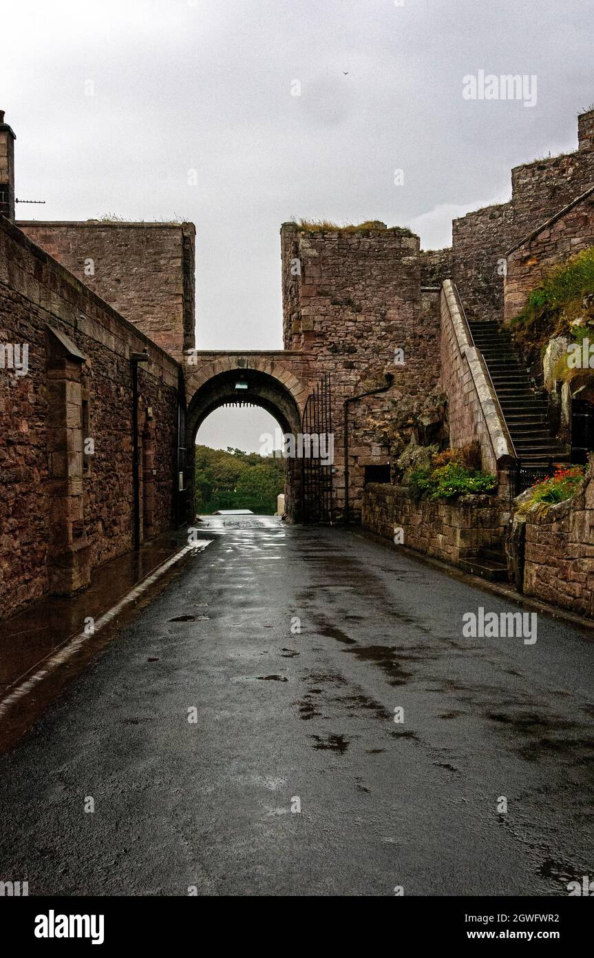 A smooth path leads an arched gateway with po0rtcullis, part of the defensive structures preventing an attack on the inner courtyard of Bamburgh Cast Stock Photo