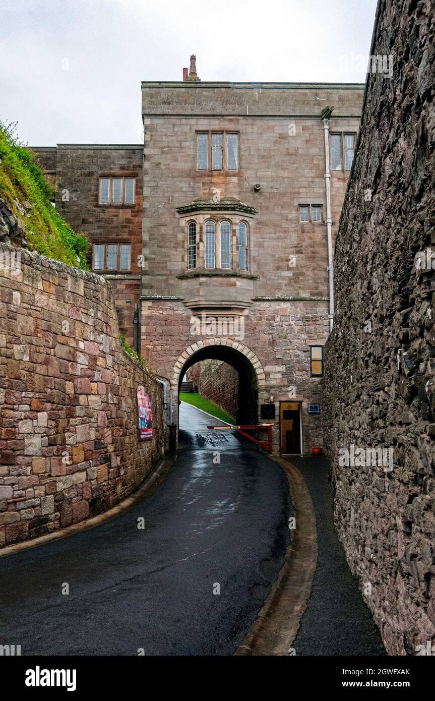 A steep hill between high stone curtain walls leads to an archway through a residential block of Bamburgh Castle controlled by a gatehouse Stock Photo