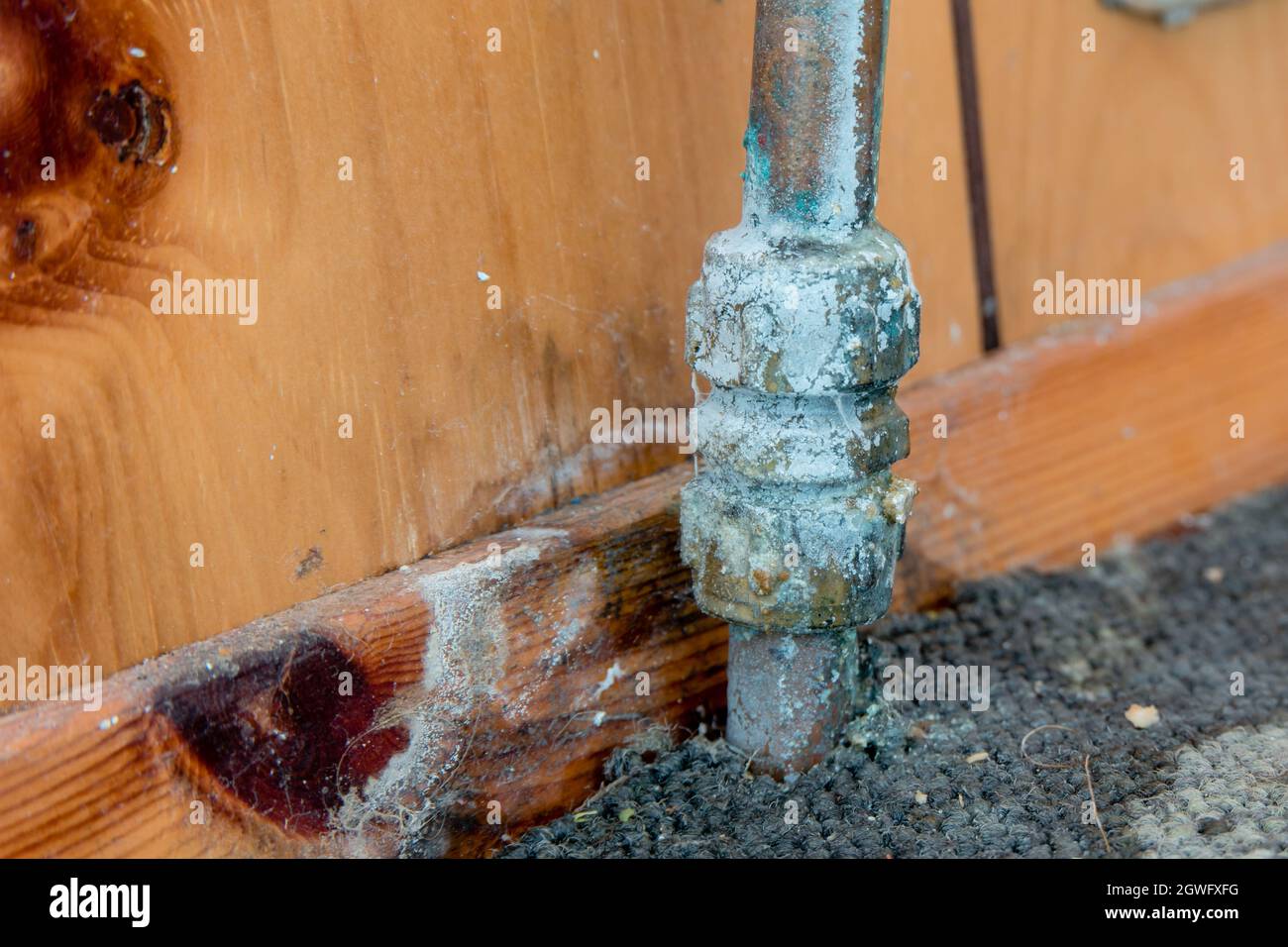 Old leaking pipe with water and limescale damage on old carpet and wood panelling Stock Photo