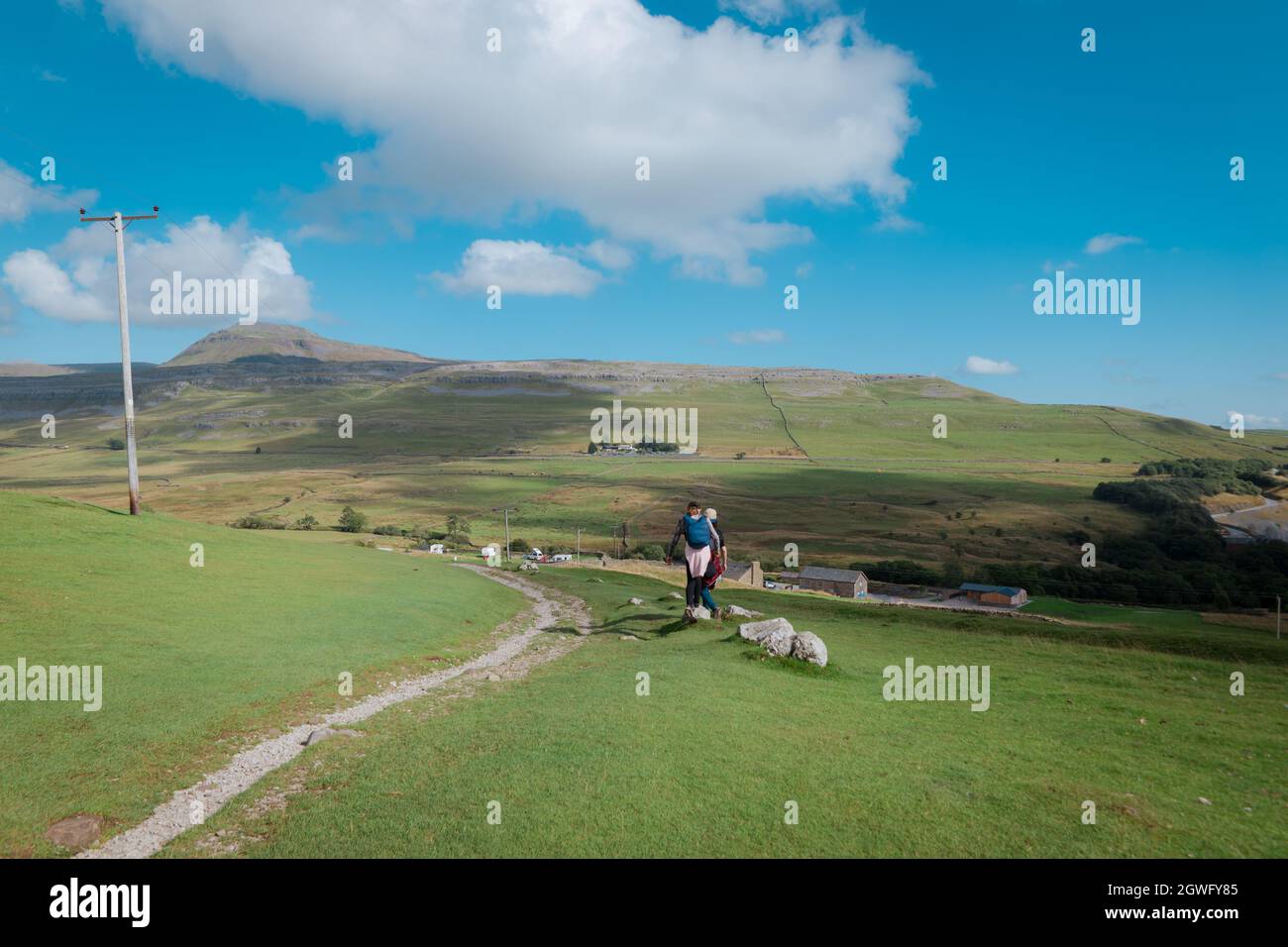 Walkers on Twistleton Lane, a roman road, with landscape views of Ingleborough peak and White Scar Cave in the Yorkshire Dales Stock Photo