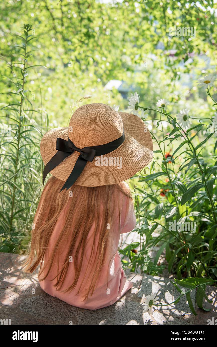 Little girl in a straw hat surrounded by flowers. Portrait of the happy ...