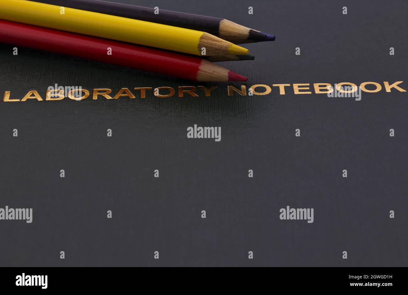 Colored pencils placed on gold lettered, dark scientific Laboratory Notebook reflect university, research, and educational emphasis on careful notatio Stock Photo