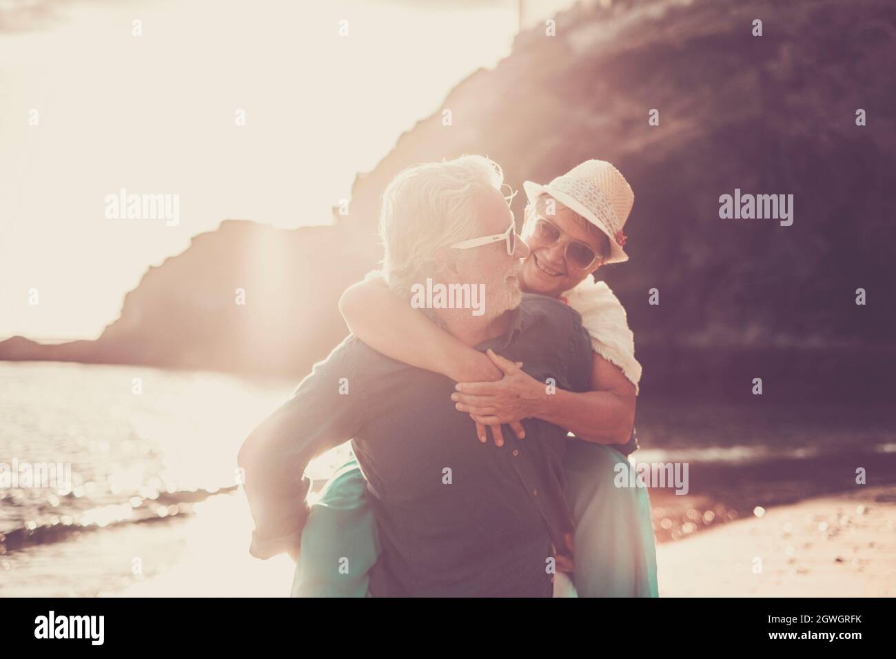 Senior couple enjoying at beach, Senior man carrying his wife on his back and having fun during summer holiday. Old woman enjoying piggyback ride on b Stock Photo
