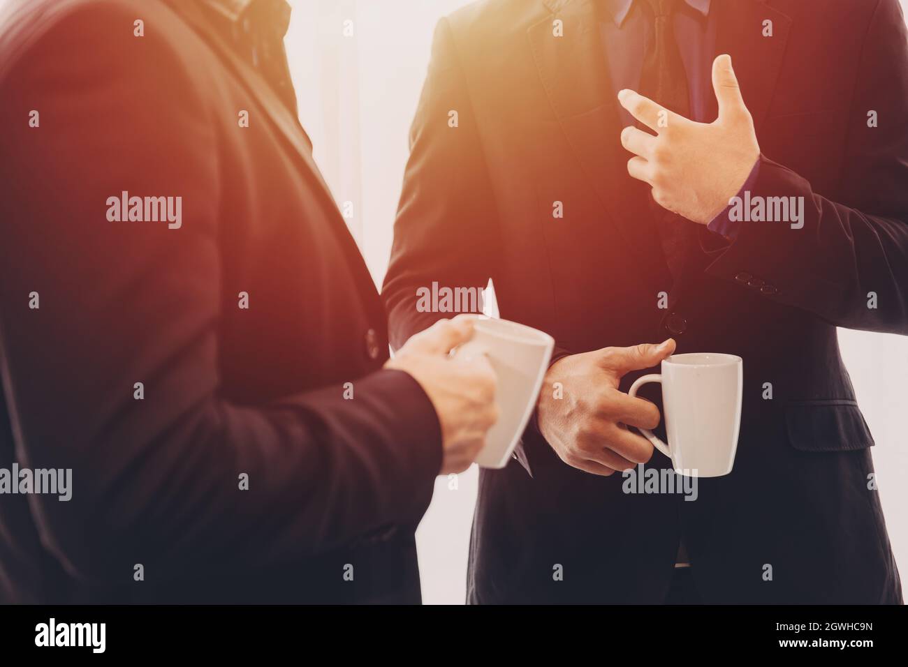 Two Business people standing talking discussion together with morning coffee mug in hand. Stock Photo