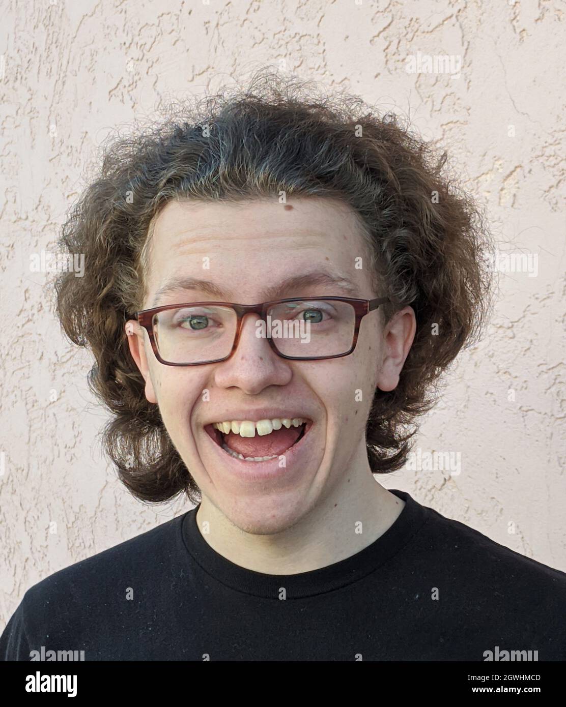 Portrait Of Smiling Teenage Boy With Curly Hair And Glasses Against Wall  Stock Photo - Alamy