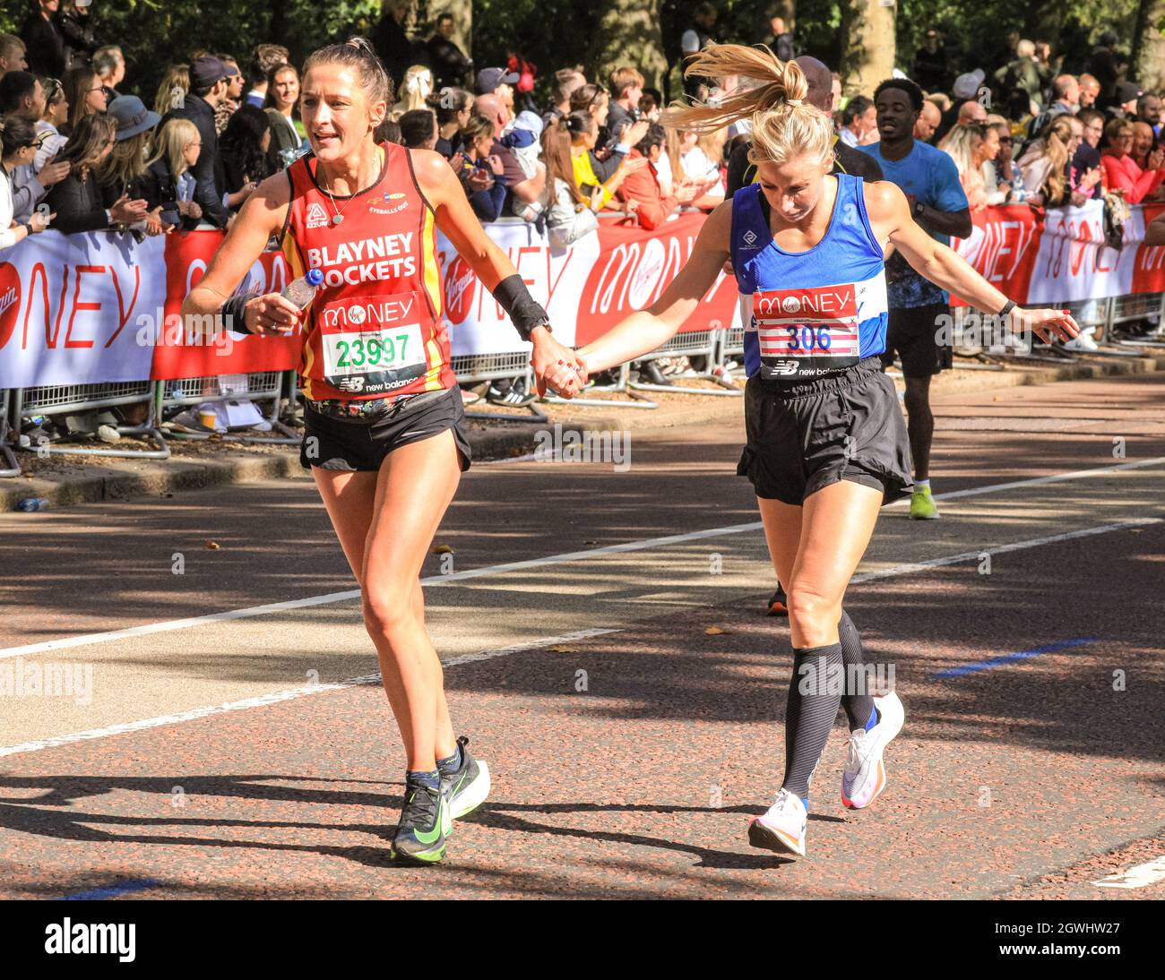 London, UK. 03rd Oct, 2021. A tired, exhausted runner is held by the hand  and helped along by a fellow participant. Mass race runners, many in  costume, on the last mile at