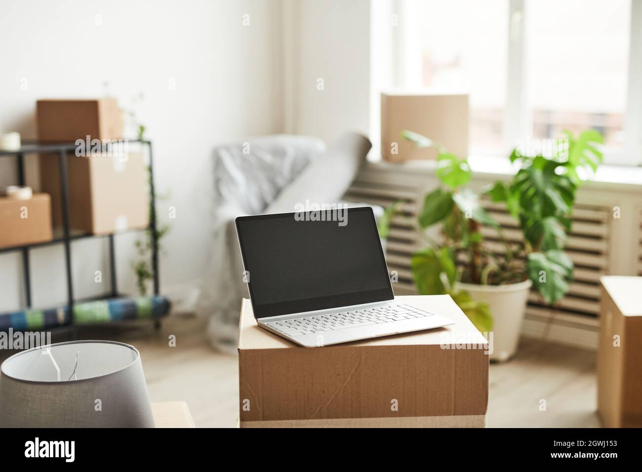 Background image of opened laptop with blank screen on cardboard boxes in new home, moving and relocation concept, copy space Stock Photo