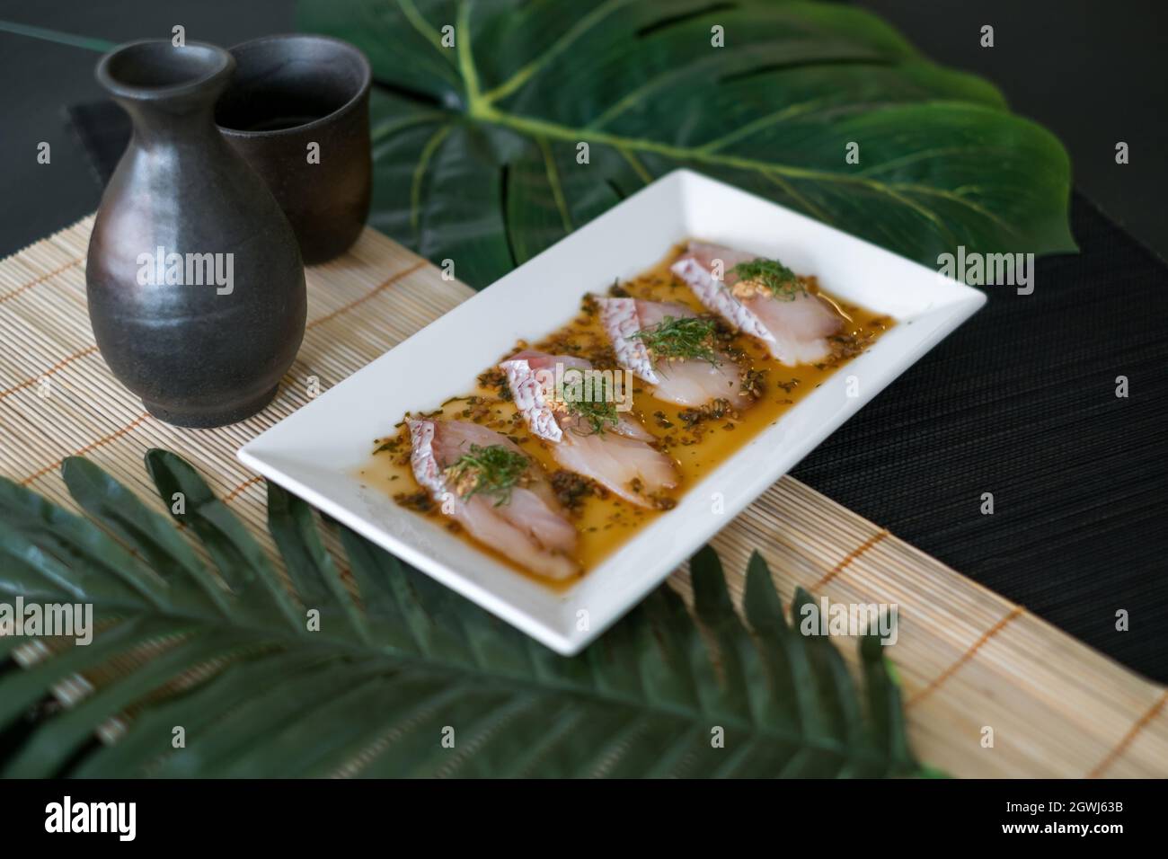 Sea bass sashimi with sauce on white plate, black decanter with sake