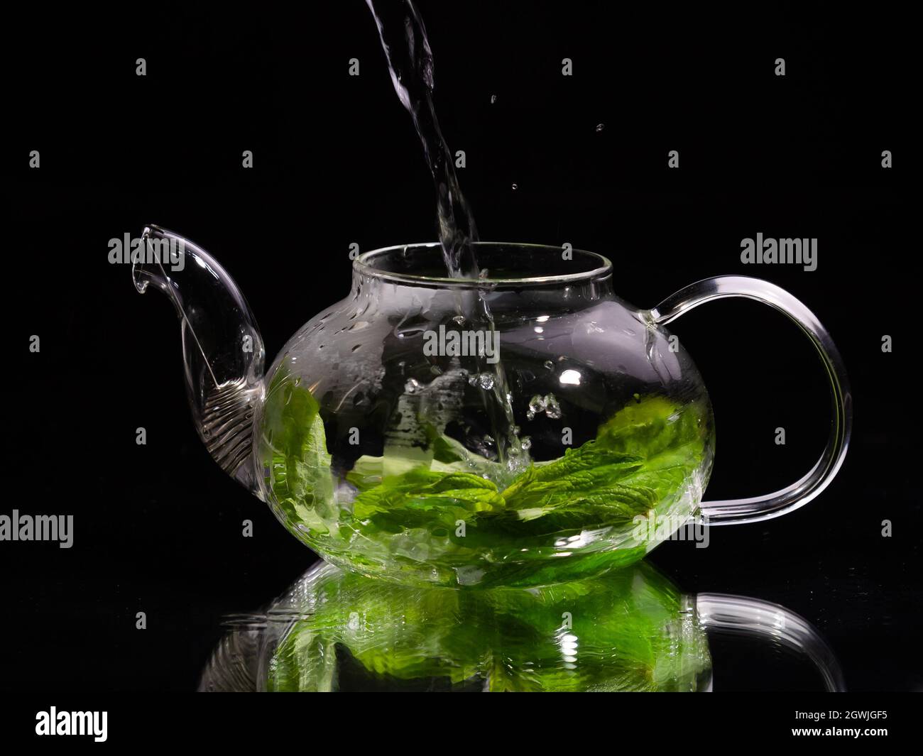 Pouring hot water into a glass teapot on a black background, green mint