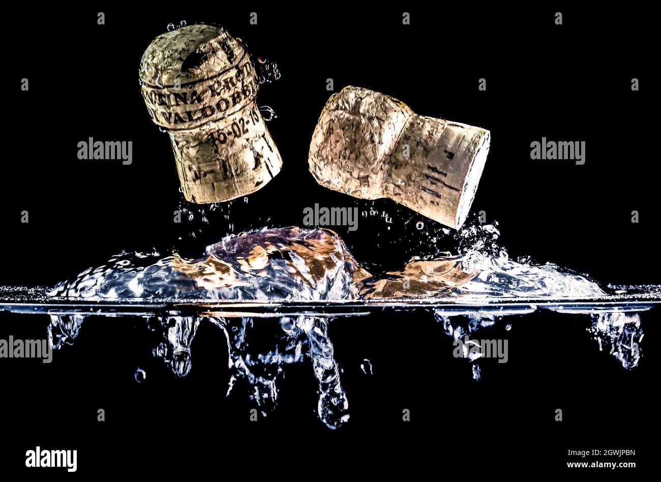 Two cork plugs flying through the water surface, splashing water on a black background. Prosecco wine plugs from the Valdobbiadene region, Italy. Stock Photo