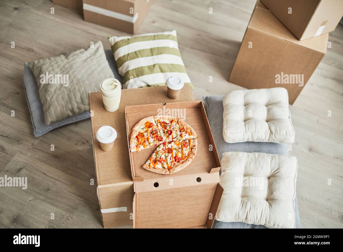Top view background image of pizza on cardboard box as makeshift table in empty room while family moving in to new house, copy space Stock Photo