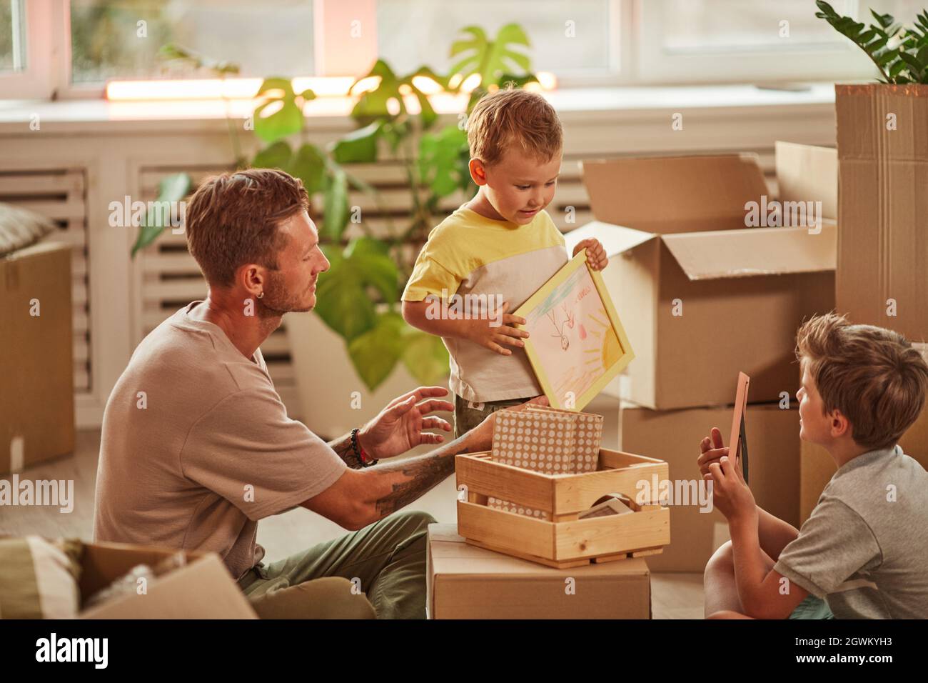 Portrait of father with two sons unpacking boxes while moving in to new home, copy space Stock Photo