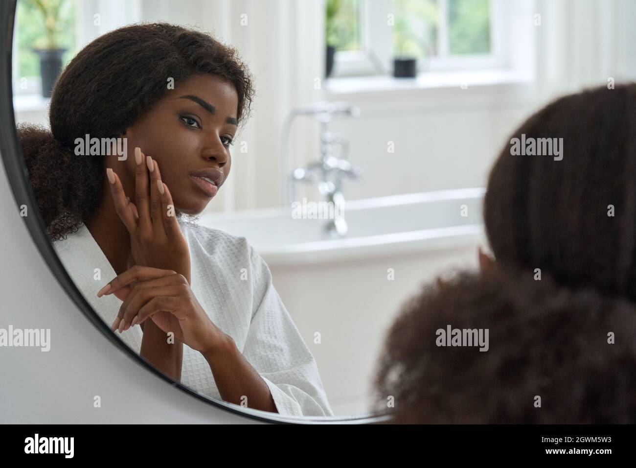 Attractive black young woman touching face skin looking in mirror. Stock Photo