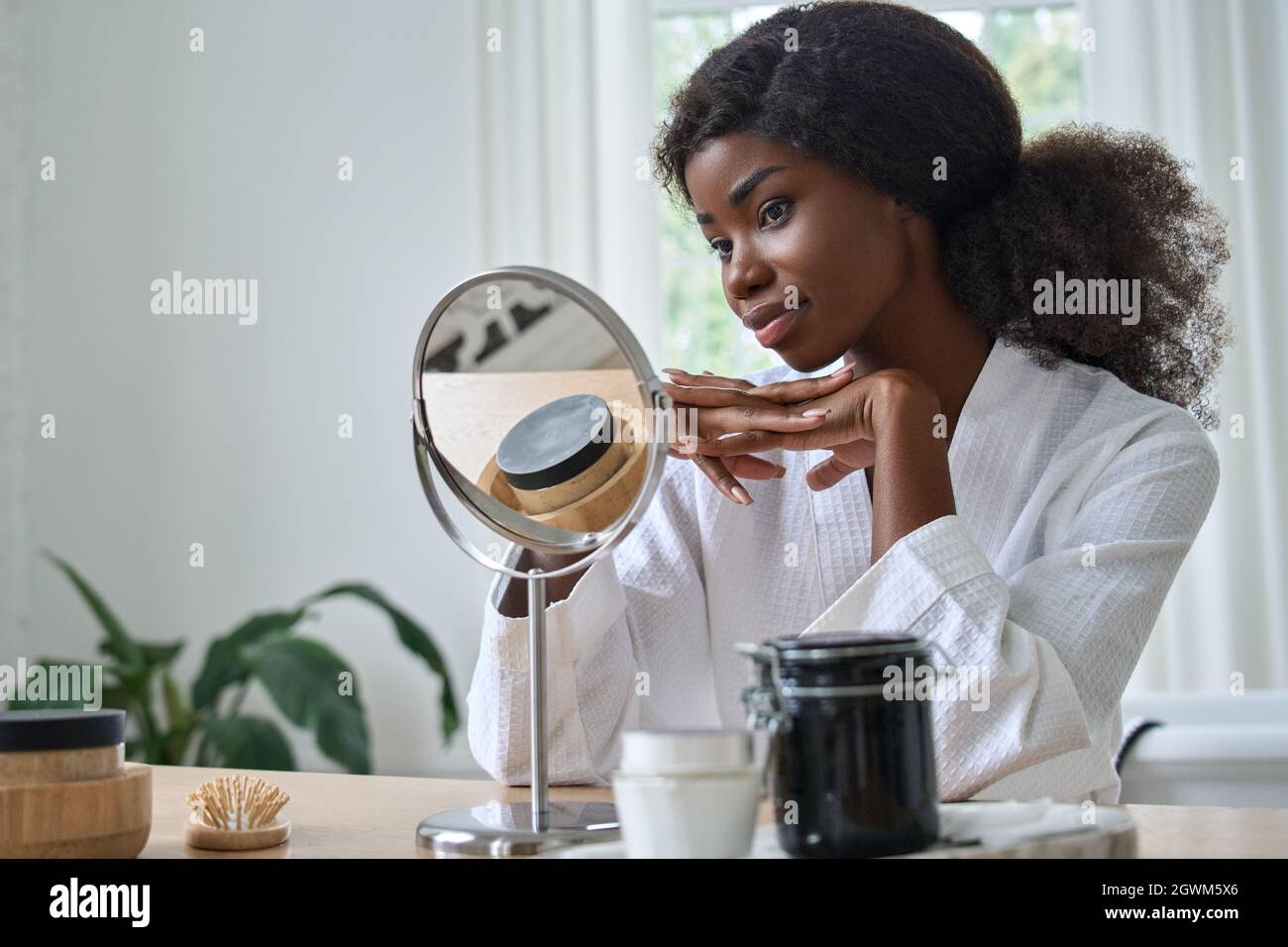 Happy pretty black young woman looking in mirror doing makeup. Stock Photo