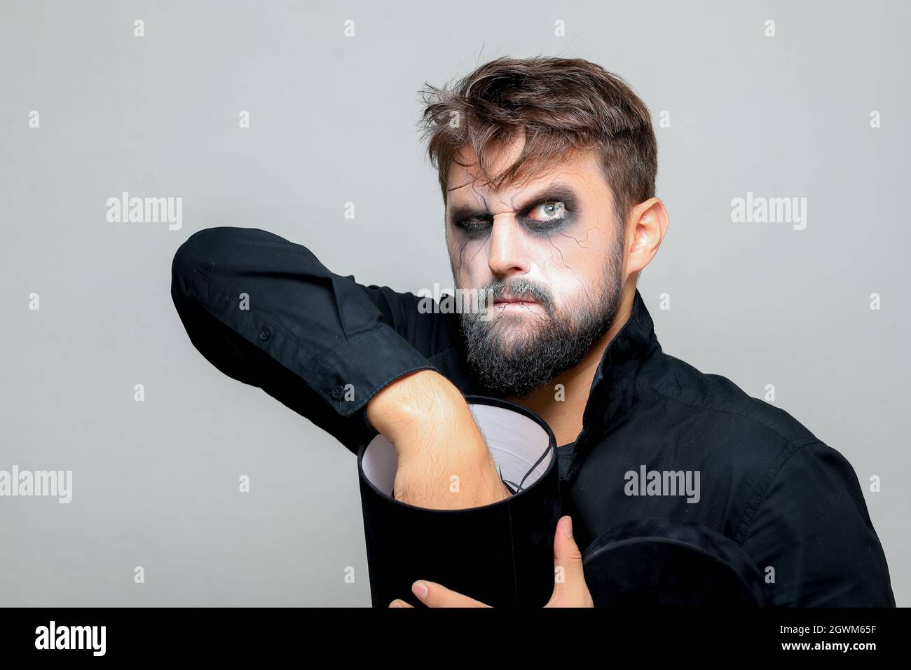 a man with a beard and makeup for Halloween holds a black box with gifts in his hands Stock Photo