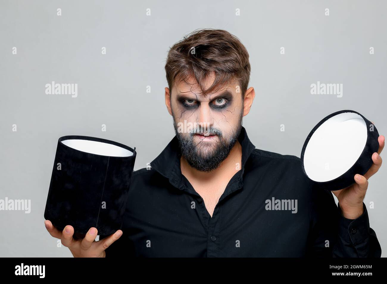 a man with a beard and makeup for Halloween holds a black box with gifts in his hands Stock Photo