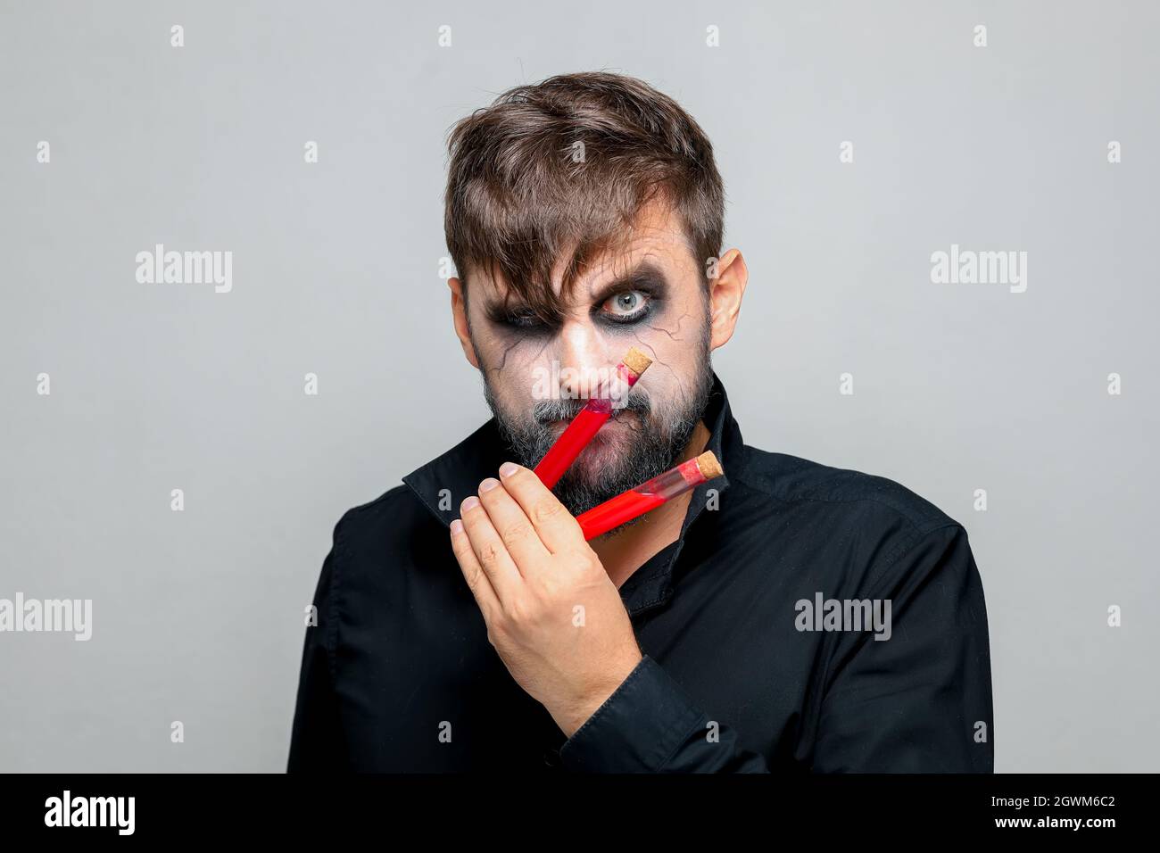 a bearded man with undead makeup for Halloween holds test tubes in ...