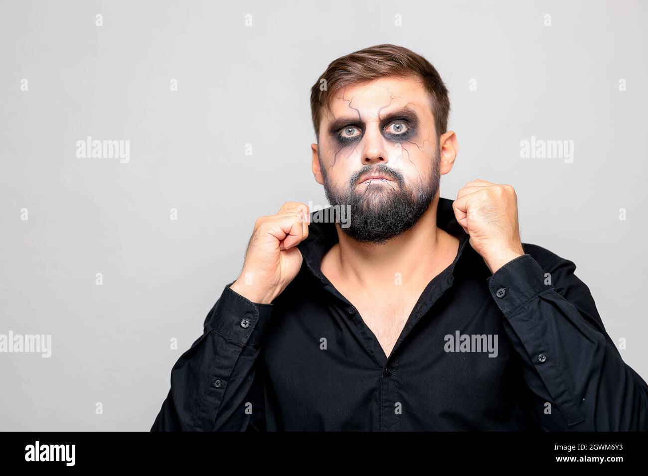 a man in a black shirt stands on a white background who has undead-style makeup for Halloween Stock Photo