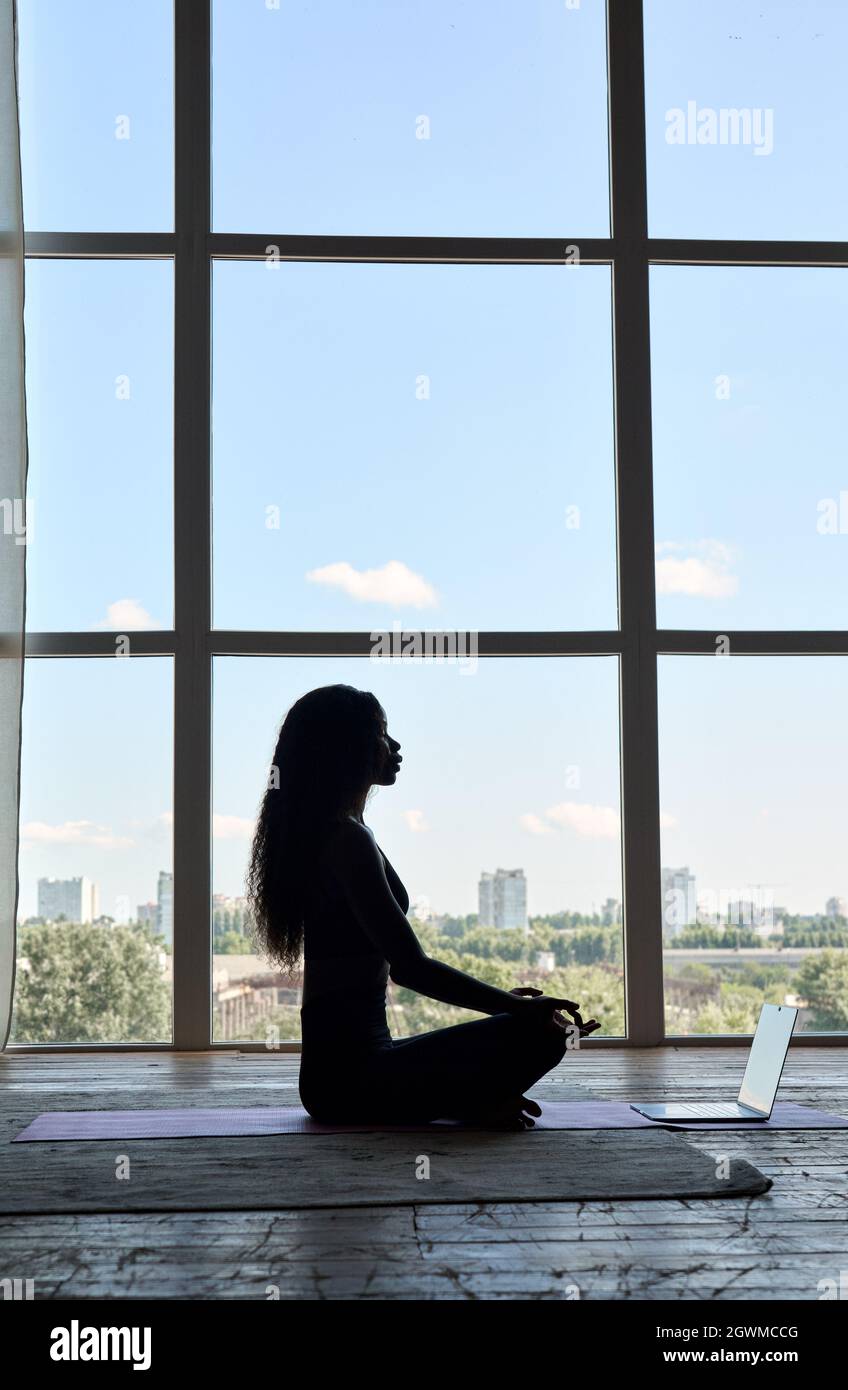 Young healthy Afro American girl silhouette on online yoga class sitting on mat. Stock Photo