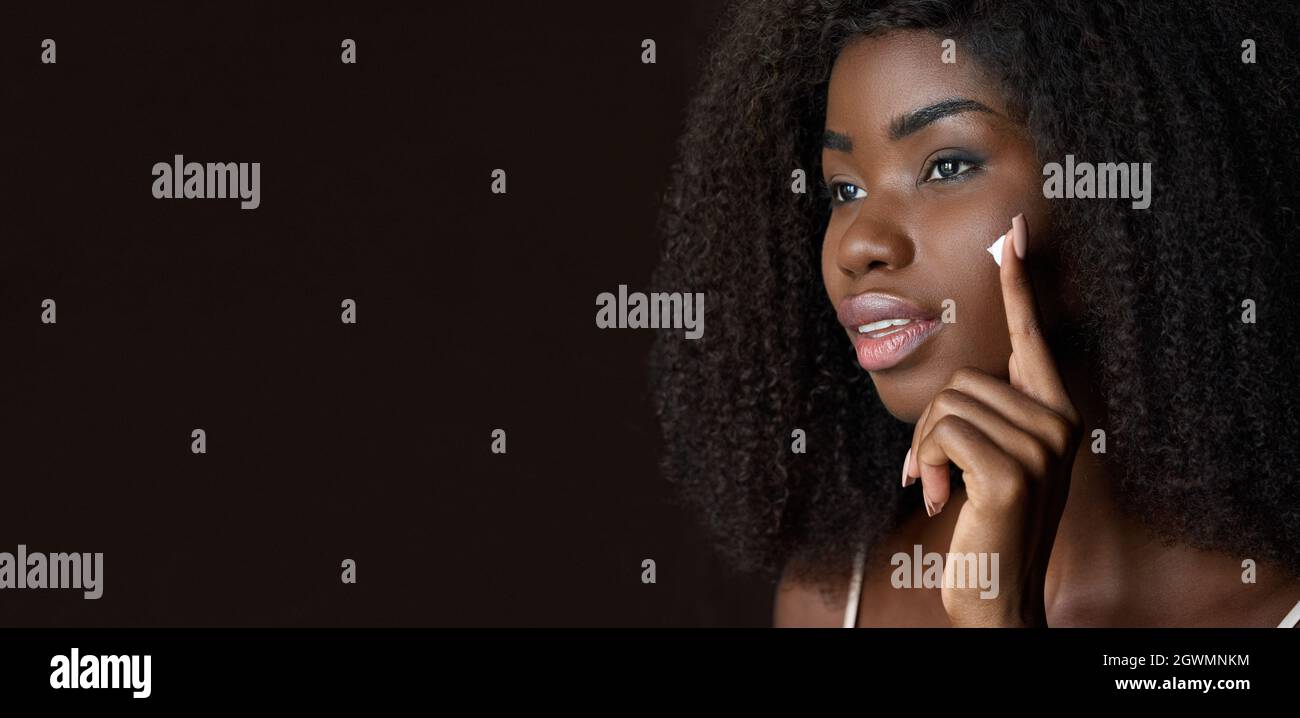 Young black woman applying face cream isolated on background. Banner Stock Photo