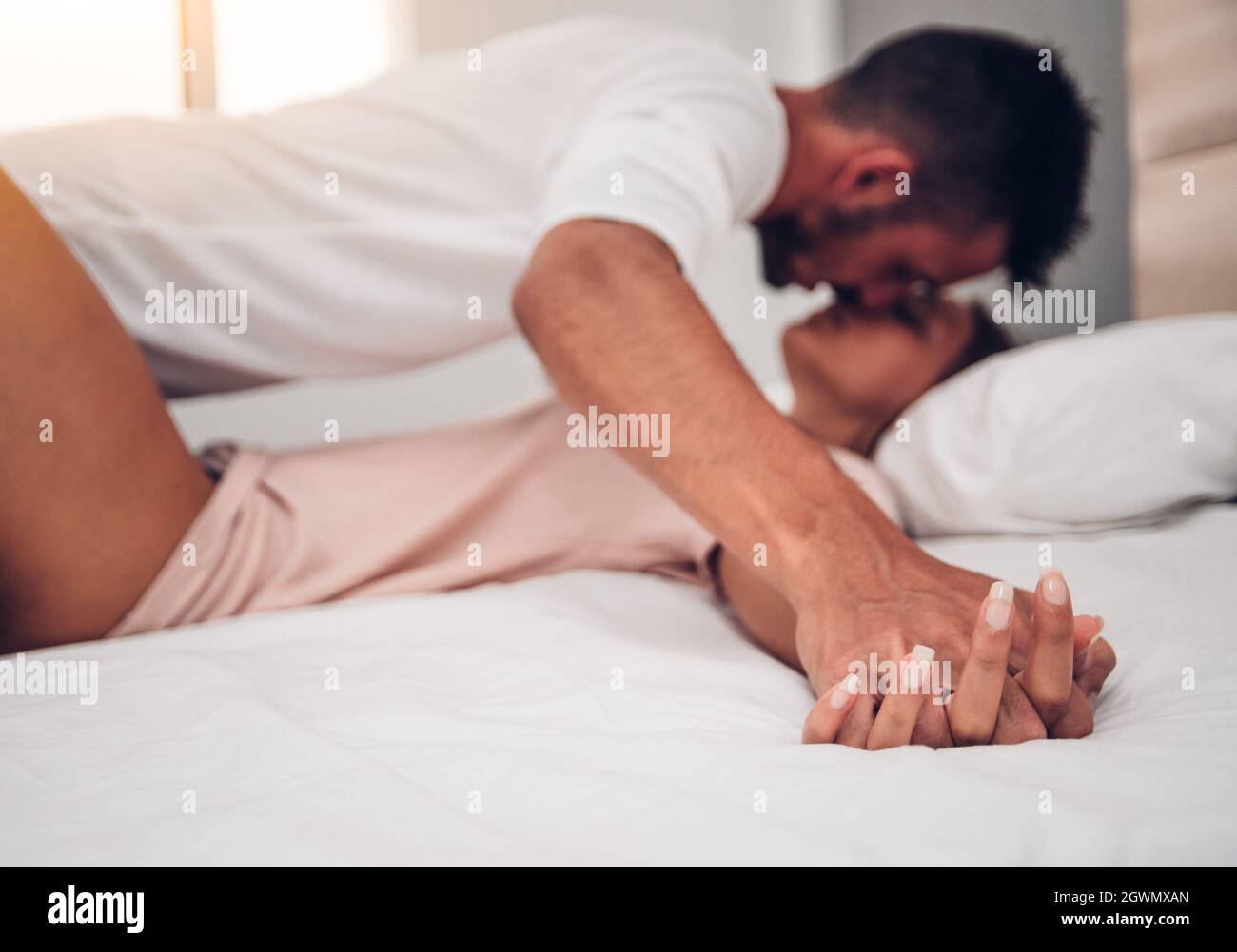 Side View Of Romantic Couple Holding Hands While Kissing On Bed Stock Photo