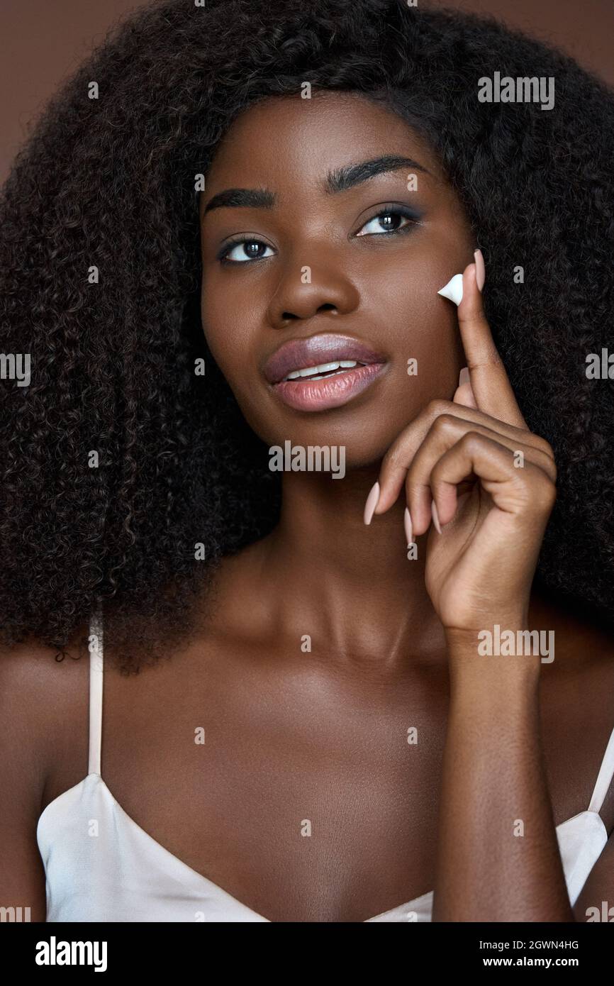 Beautiful happy young black girl applying putting cream. Skincare concept. Stock Photo