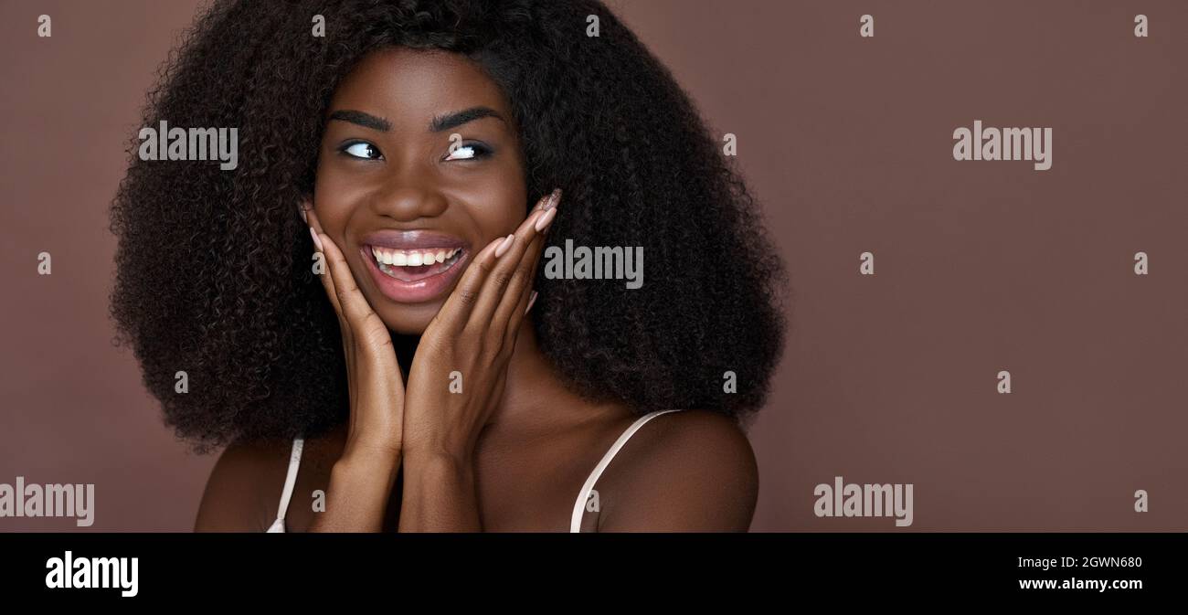 Happy black young woman touching healthy smooth face skin on brown background. Stock Photo