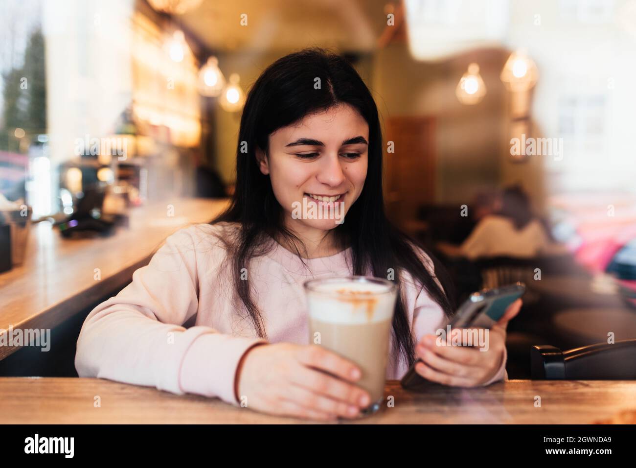 Girl Smiling, Drinks Coffee In Cafe And Reading Phone. Blurred Background. High Quality Photo Stock Photo