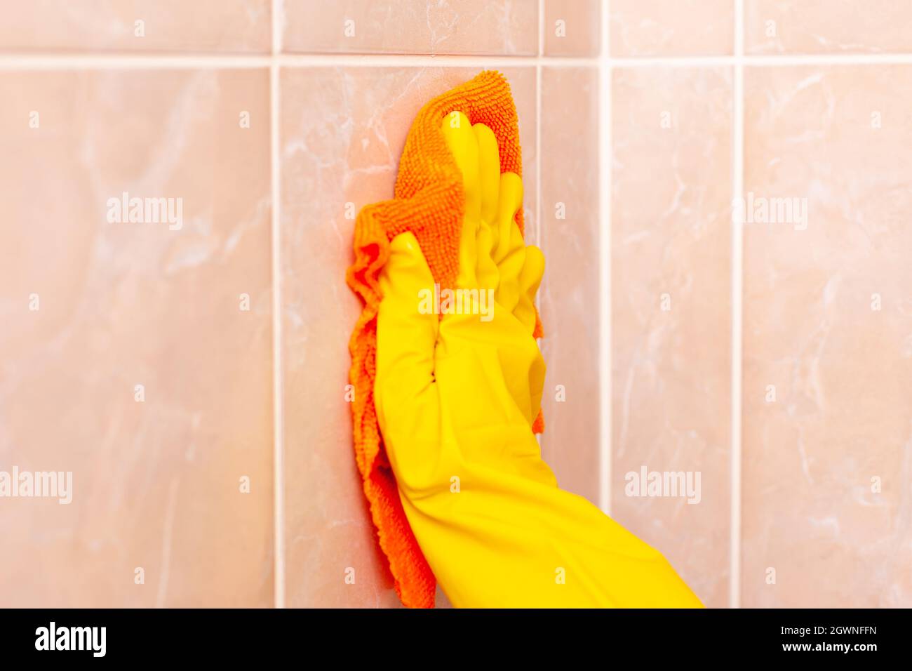 hand in a yellow rubber glove wipes the tiles in the bathroom Stock ...