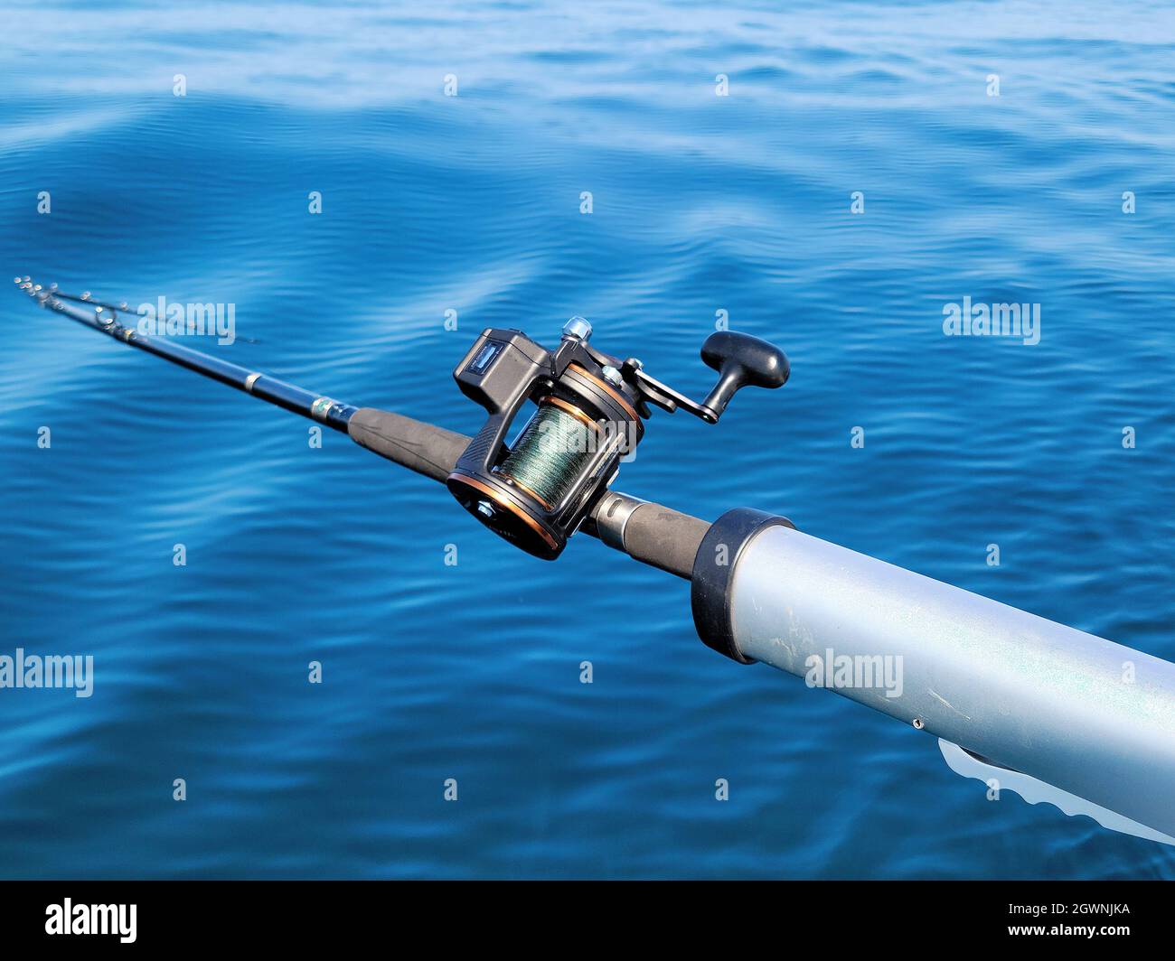 Fishing pole with reel in blue lake water Stock Photo