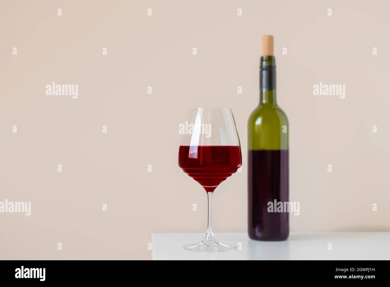 Red wine glass with dark wine bottle on white table. Simple interior with copy space Stock Photo