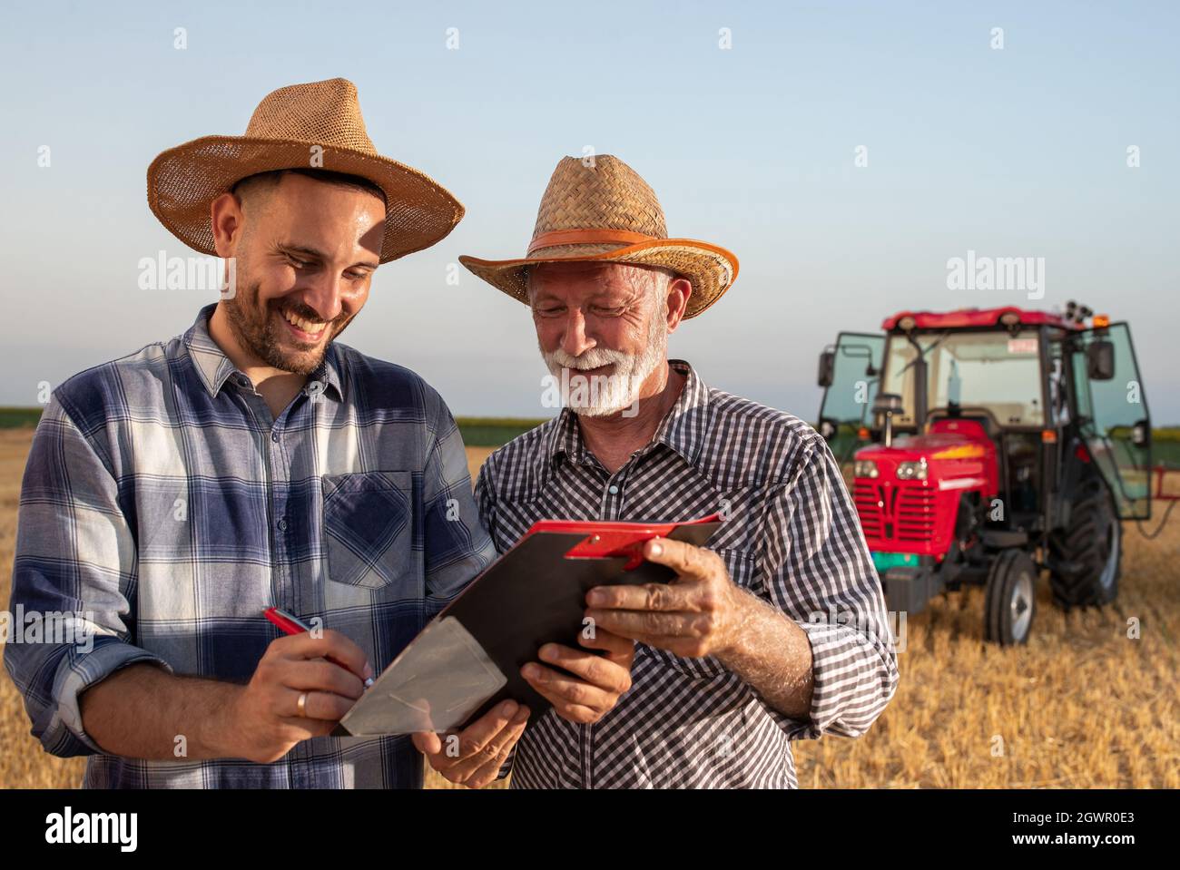 Satisfied farmer signing contract standing in harvested field smiling. Elderly insurance sales