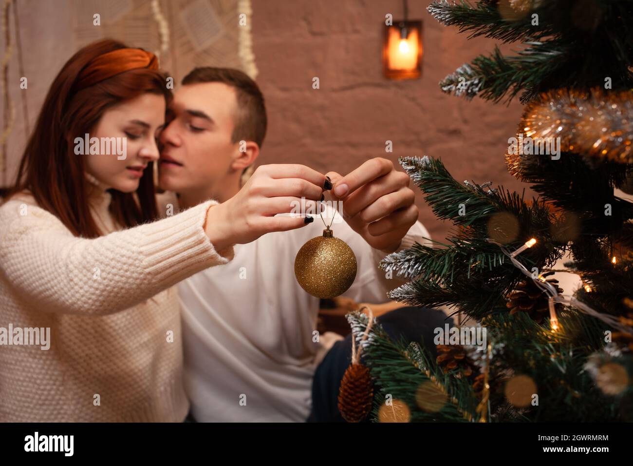 Young People In Love Hang A Toy On The Christmas Tree. A Guy And A Girl  Dress Up A Christmas Tree Stock Photo - Alamy