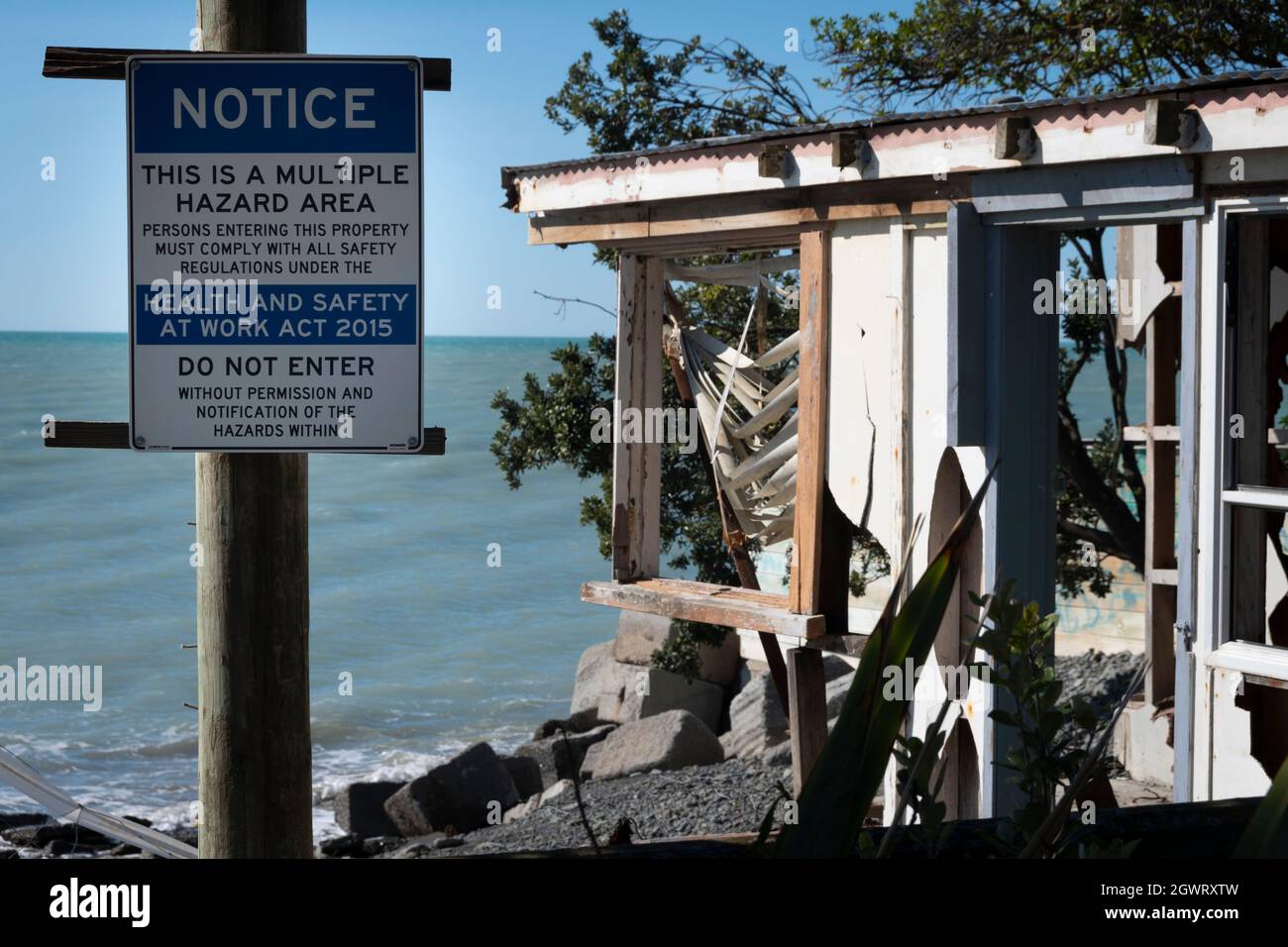 Hazard sign in front of house destroyed by coastal erosion and rising