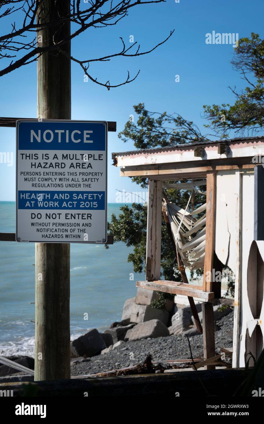 Hazard sign in front of house destroyed by coastal erosion and rising
