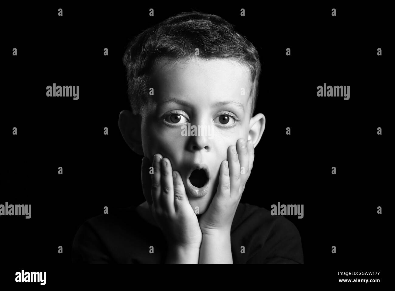 Black and white portrait of surprised little boy on dark background Stock Photo
