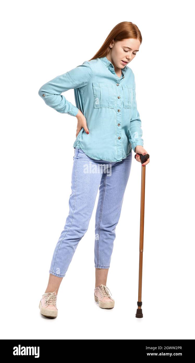Sick young woman with walking stick suffering from back pain on white