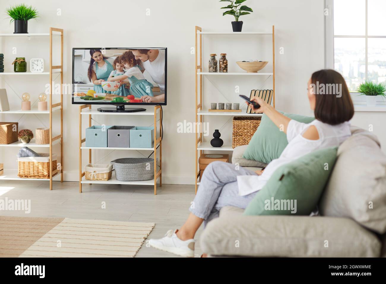 Woman sitting on sofa at home and switching on her television set with big screen Stock Photo