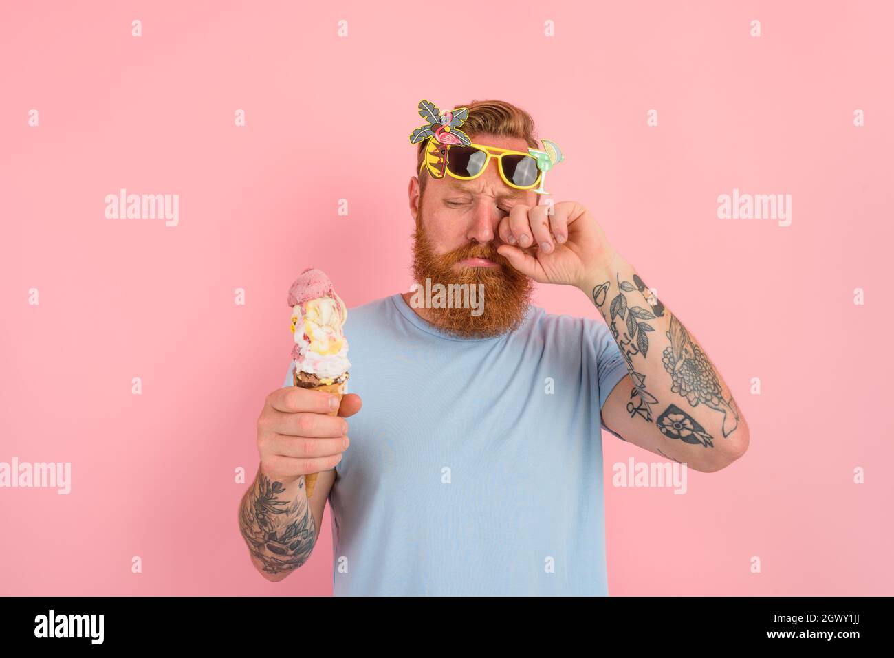 Cry man with beard and tattoos eats a big icecream Stock Photo