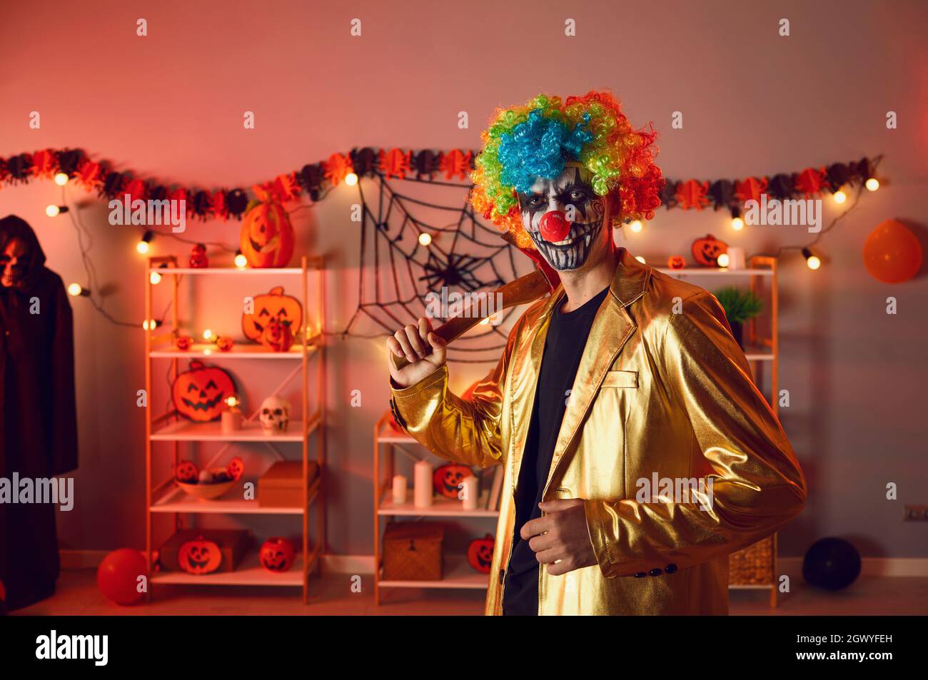 Portrait of adult man dressed up as creepy evil clown with axe at Halloween party Stock Photo